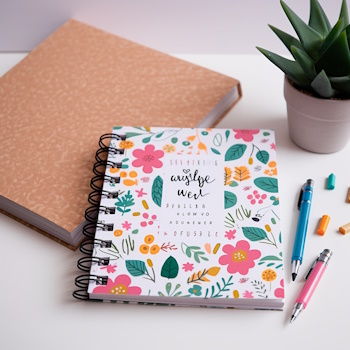 Cuaderno floral con bolígrafos, cerca de planta